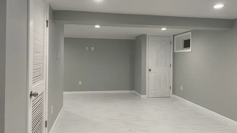 A finished basement with gray walls, recessed lights and a white marble-look tile floor