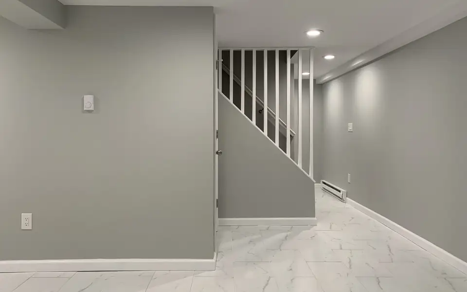 A finished basement with gray walls, recessed lights, a marble-look tile floor and a white stair rail